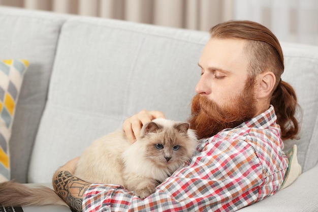 Joven barbudo con gato esponjoso sentado en el sofá