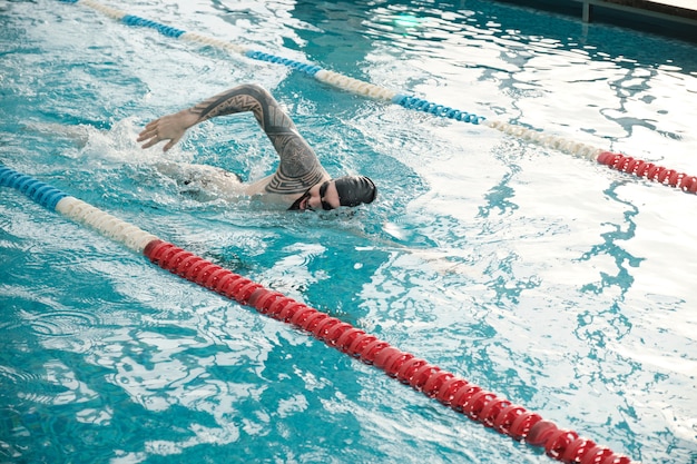 Joven barbudo con gorra y gafas de natación en piscina moderna