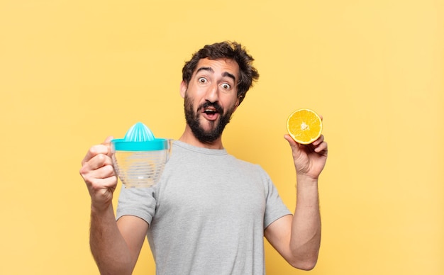 Joven barbudo haciendo dieta expresión de sorpresa y sosteniendo una naranja