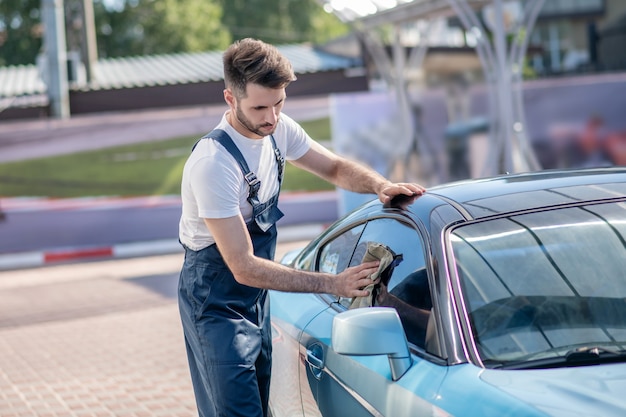 Joven barbudo limpiando el cristal del coche