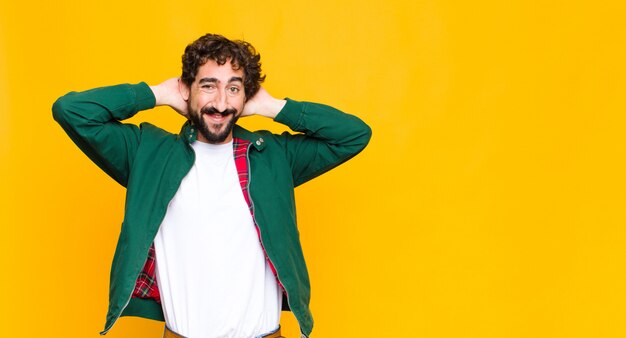 Joven barbudo loco que parece feliz, despreocupado, amable y relajado disfrutando de la vida y el éxito, con una actitud positiva contra la pared