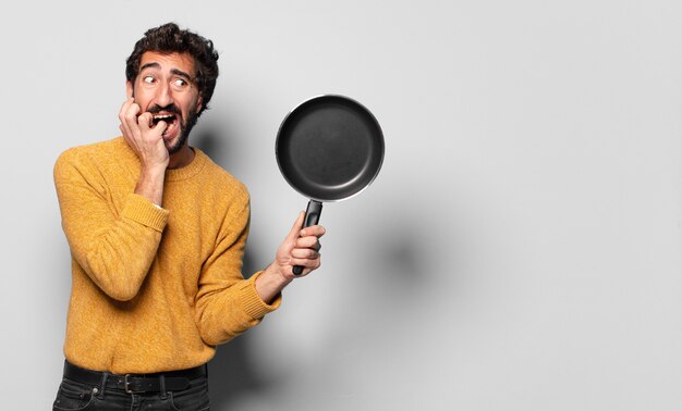 Joven barbudo loco con una sartén. concepto de cocina