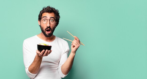 Joven barbudo loco con un tazón de ramen de fideos