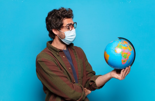 Joven barbudo con máscara médica y modelo de mapa del mundo