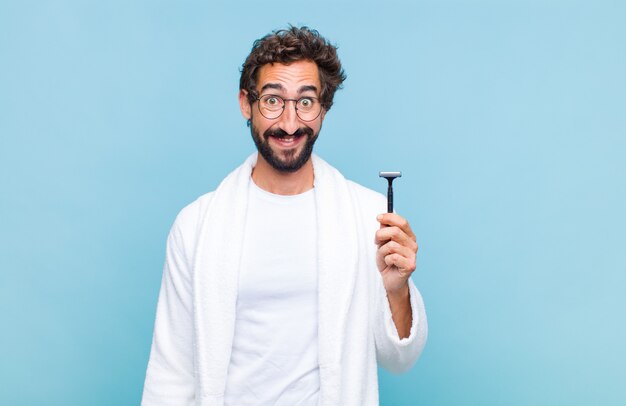 Joven barbudo que parece feliz y gratamente sorprendido, emocionado con una expresión fascinada y conmocionada