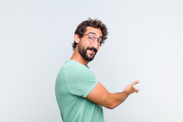 Joven barbudo que se siente feliz y alegre, sonriendo y dándote la bienvenida, invitándote con un gesto amistoso