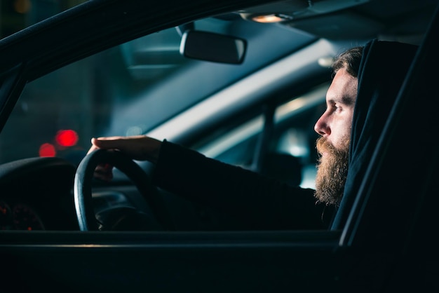 Un joven barbudo sentado en un coche visto a través de la ventana por la noche