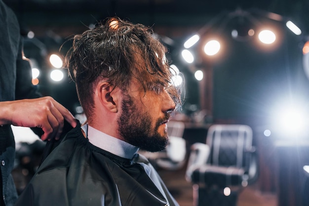 Joven barbudo sentado y cortándose el pelo en la peluquería