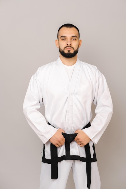 Un joven barbudo serio con uniforme de taekwondo sostiene su cinturón negro