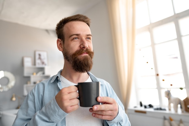 Joven barbudo sonriendo y bebiendo café en casa