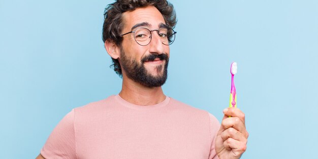 Joven barbudo sonriendo felizmente con una mano en la cadera y actitud confiada, positiva, orgullosa y amistosa