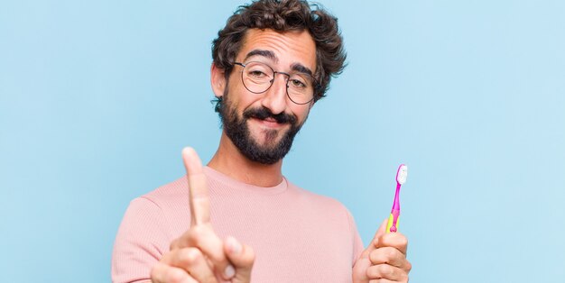 Joven barbudo sonriendo con orgullo y confianza haciendo la pose número uno triunfalmente, sintiéndose como un líder