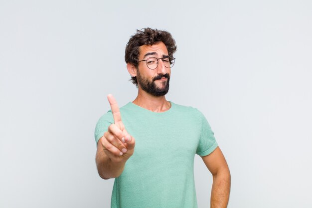 Joven barbudo sonriendo con orgullo y confianza haciendo la pose número uno triunfalmente, sintiéndose como un líder