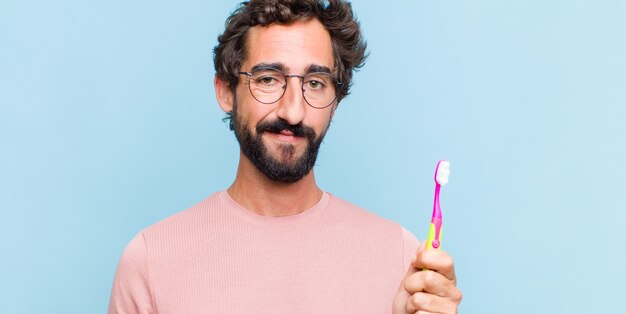 Joven barbudo sonriendo positivamente y con confianza, luciendo satisfecho, amigable y feliz