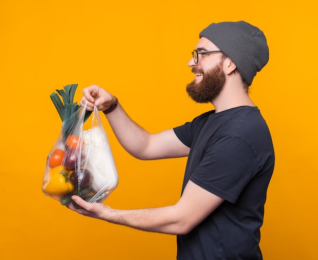 Un joven barbudo sostiene una bolsa con algunos comestibles y sonríe los está regalando.