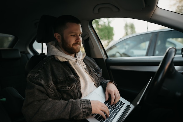 Un joven barbudo con su computadora portátil dentro de un auto confort