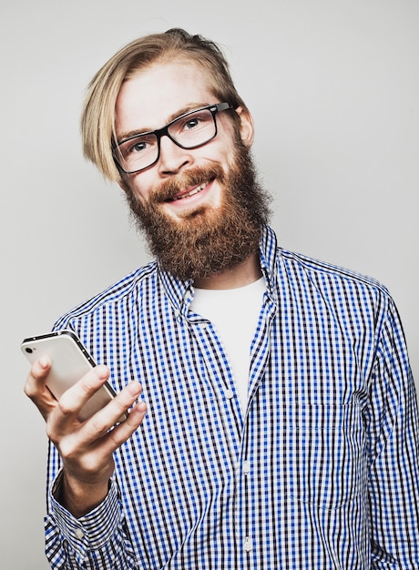 joven barbudo con teléfono móvil en mano en gris.