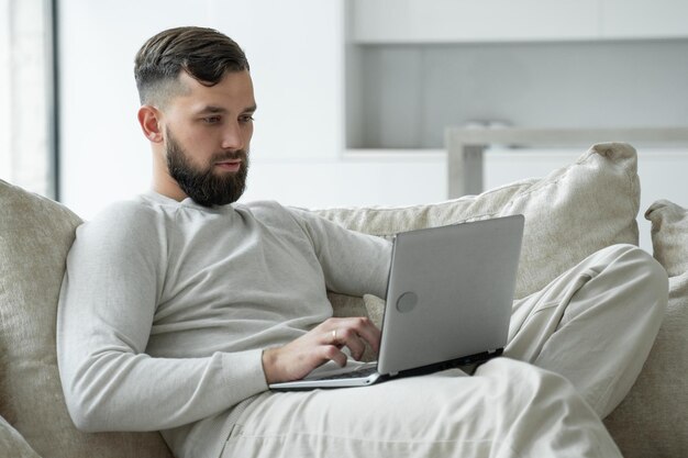 Joven barbudo usa una computadora portátil para trabajar en casa en la sala de estar