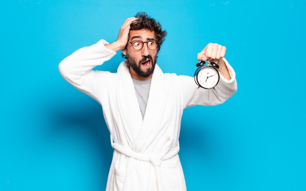 Joven barbudo vestido con albornoz y un reloj despertador