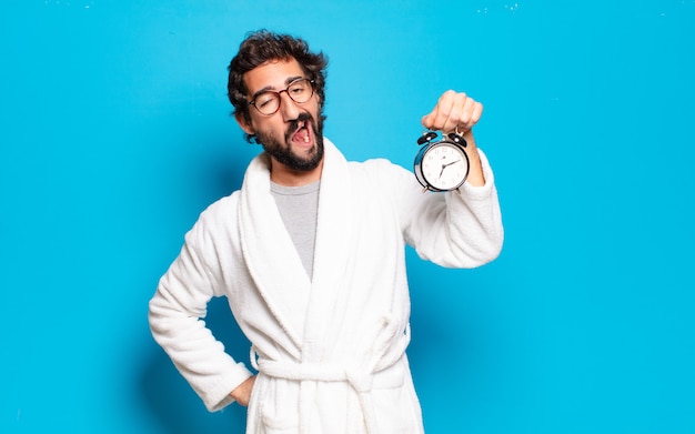 Joven barbudo vestido con albornoz y un reloj despertador