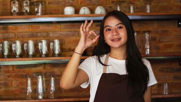 Joven barista asiática llevar delantal gesto OK