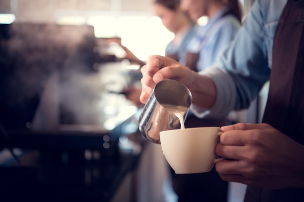 Joven barista experto en la elaboración de café campeón creando arte latte en una taza de café para un cliente