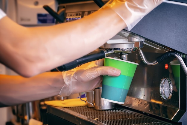 Joven barista hace café en la máquina de café con guantes de látex, cumpliendo con las normas de seguridad de higiene al preparar alimentos