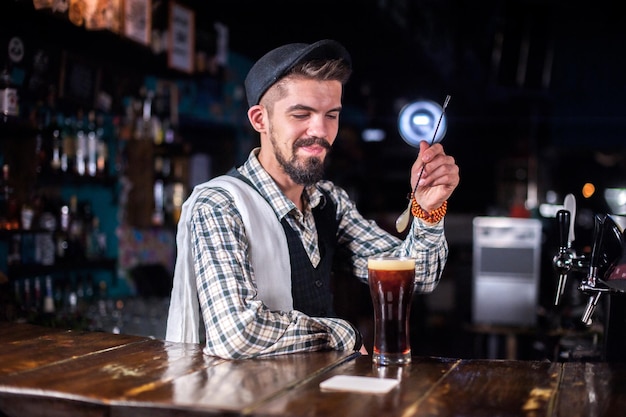 El joven barman hace un cóctel mientras está parado cerca del mostrador del bar en el bar