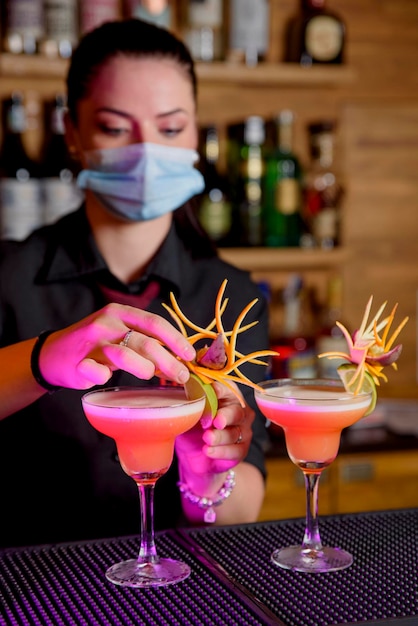 Joven bartender hace cóctel con mascarilla médica y protección contra el coronavirus COVID-19.