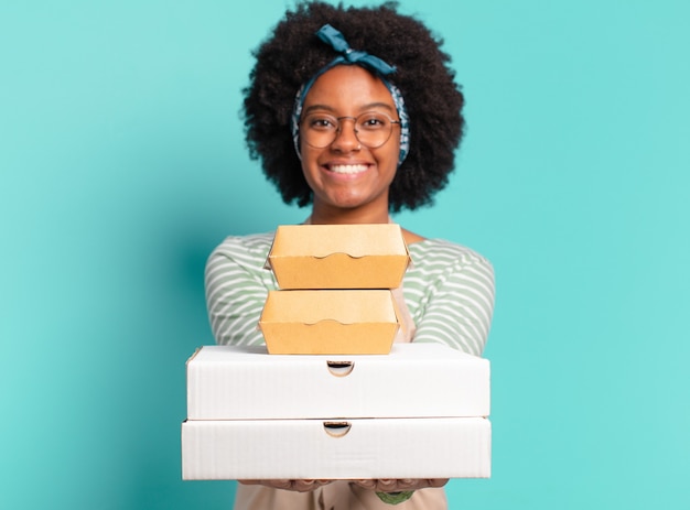 Joven bastante afro entregar a mujer con cajas de pizza y hamburguesas para llevar