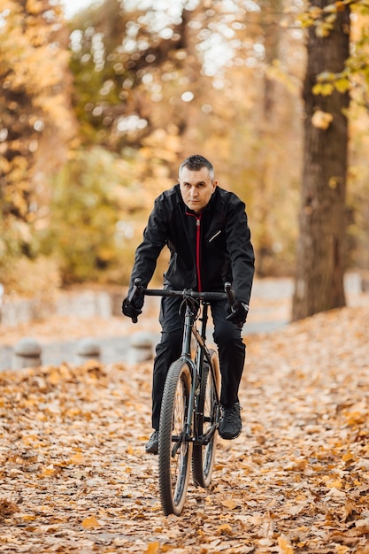 Joven bastante atlético parado con bicicleta en el parque de otoño