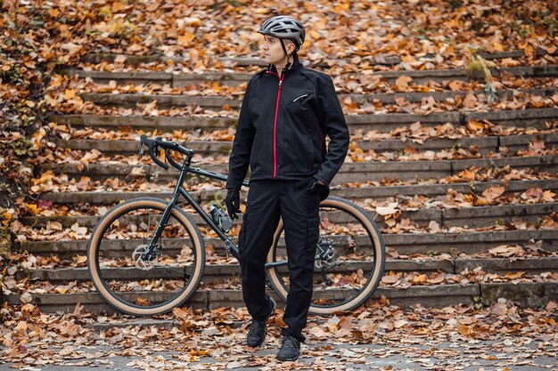 Joven bastante atlético parado con bicicleta en el parque de otoño