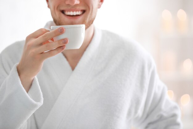 Joven en bata de baño tomando café en casa