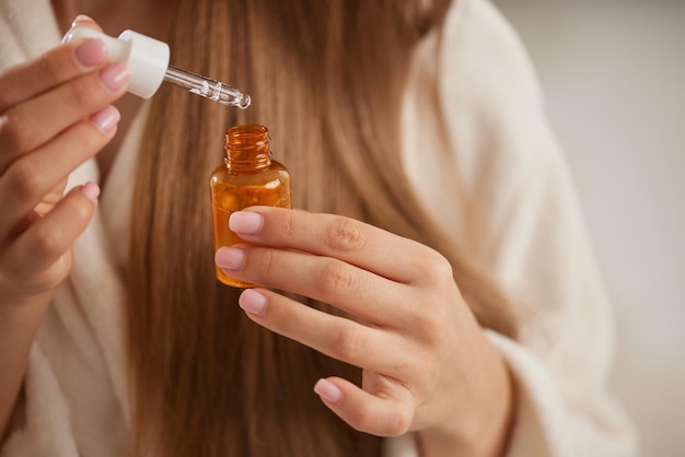 Una joven con bata blanca aplica vitaminas a su cabello en casa el concepto de cuidado del cabello