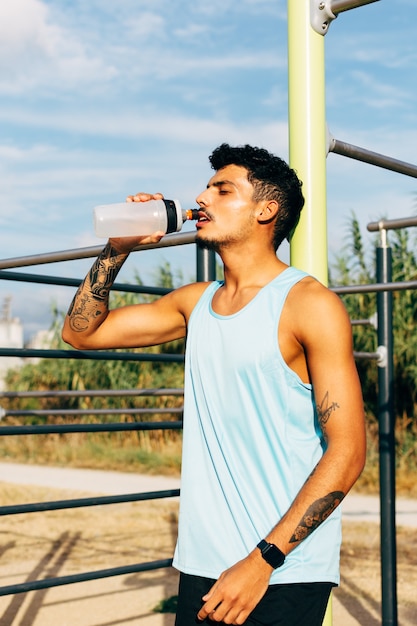 Joven bebe agua después de hacer ejercicio en la barra horizontal al aire libre