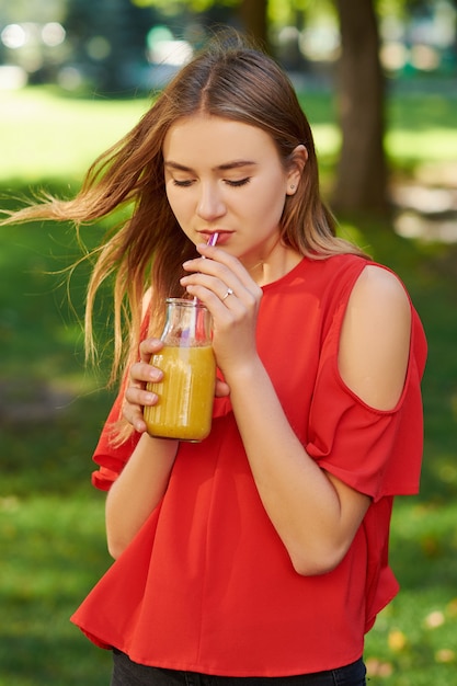 Foto joven bebe batido de desintoxicación saludable con jugo en el fondo del parque verde. superalimentos, salud, frescura de verano, concepto de comida vegetariana