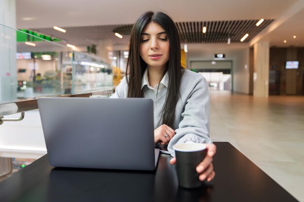 Una joven bebe café mientras trabaja en una computadora portátil