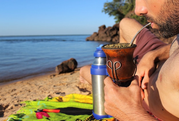 Foto un joven bebe mate en la playa del río paraná