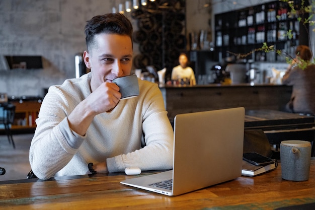 Foto joven bebe té y trabaja en una computadora portátil, trabajador independiente que trabaja en un café