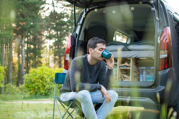 Joven bebiendo café junto a su autocaravana Tiempo de relajación en la naturaleza