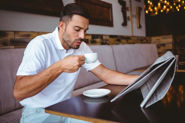 Joven bebiendo café leyendo periódico