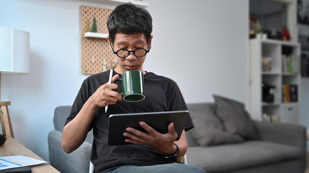 Joven bebiendo café y revisando noticias en la mesa digital en casa