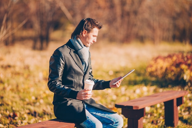 Joven bebiendo café con teléfono en otoño parque al aire libre