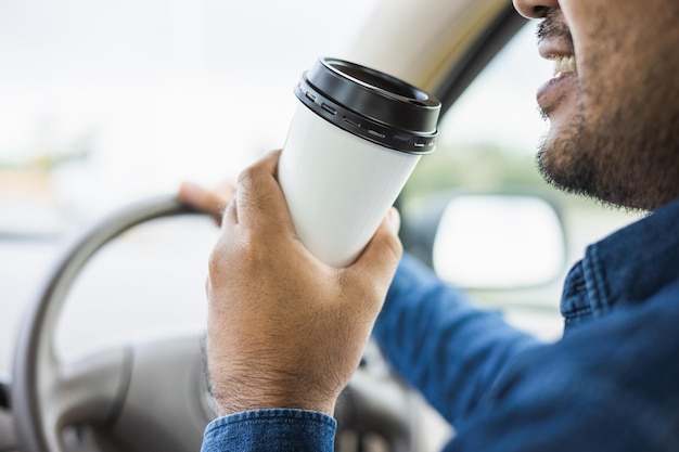 Joven bebiendo una taza de café caliente mientras conduce un automóvil para viajar Manos sosteniendo el volante