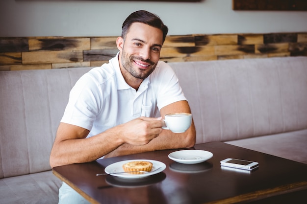 Joven bebiendo una taza de café y pastelería al lado