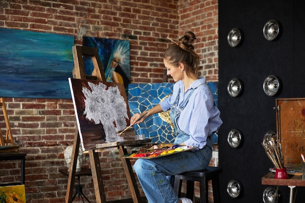 Joven y bella artista femenina pintando naturaleza muerta con girasol sobre lienzo utilizando pinturas al óleo y un ...