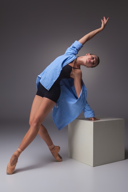 La joven y bella bailarina de estilo moderno posando en un cubo blanco sobre un fondo gris de estudio