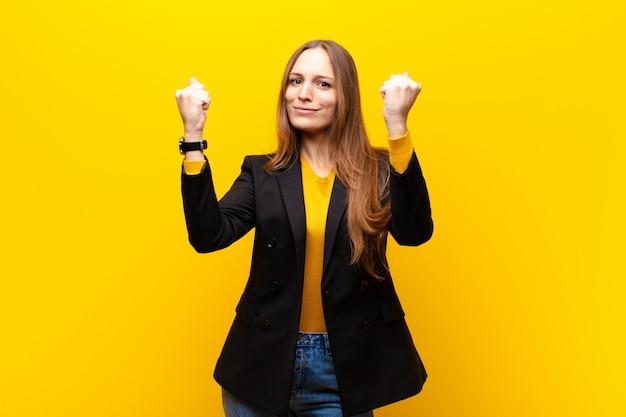 Joven y bella empresaria celebrando un éxito increíble como un ganador, luciendo emocionada y feliz diciendo ¡Toma eso! contra naranja