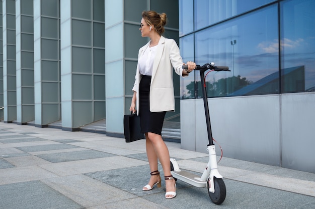 Joven y bella empresaria monta scooter eléctrico en la ciudad