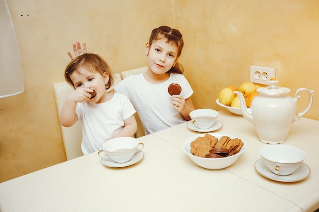 Foto joven y bella mamá en la cocina con sus hijos bebiendo té con galletas